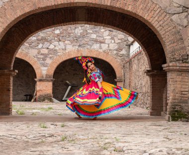 Frida 'dan esinlenerek Frida Kahlo' yu andıran Meksikalı bir kadın narin kemer yolları altında yaşlanmış bir sandalyeyi şereflendirir. Bir ışık ve gölge oyunuyla yıkandı, geleneksel kıyafetleri ve derin derin bakışları