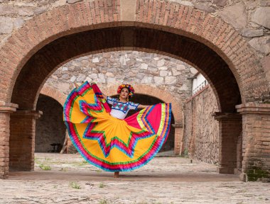 Frida 'dan esinlenerek Frida Kahlo' yu andıran Meksikalı bir kadın narin kemer yolları altında yaşlanmış bir sandalyeyi şereflendirir. Bir ışık ve gölge oyunuyla yıkandı, geleneksel kıyafetleri ve derin derin bakışları