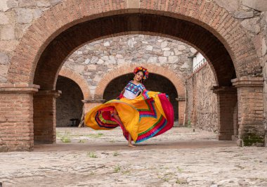 Frida 'dan esinlenerek Frida Kahlo' yu andıran Meksikalı bir kadın narin kemer yolları altında yaşlanmış bir sandalyeyi şereflendirir. Bir ışık ve gölge oyunuyla yıkandı, geleneksel kıyafetleri ve derin derin bakışları