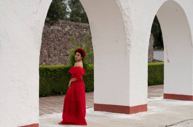 Frida 'dan esinlenerek Frida Kahlo' yu andıran Meksikalı bir kadın narin kemer yolları altında yaşlanmış bir sandalyeyi şereflendirir. Bir ışık ve gölge oyunuyla yıkandı, geleneksel kıyafetleri ve derin derin bakışları