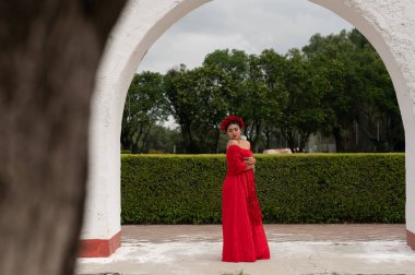 Frida 'dan esinlenerek Frida Kahlo' yu andıran Meksikalı bir kadın narin kemer yolları altında yaşlanmış bir sandalyeyi şereflendirir. Bir ışık ve gölge oyunuyla yıkandı, geleneksel kıyafetleri ve derin derin bakışları