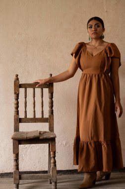 Frida 'dan esinlenerek Frida Kahlo' yu andıran Meksikalı bir kadın narin kemer yolları altında yaşlanmış bir sandalyeyi şereflendirir. Bir ışık ve gölge oyunuyla yıkandı, geleneksel kıyafetleri ve derin derin bakışları