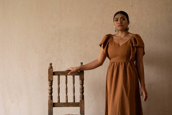 Frida-Inspired Essence: A Mexican woman, reminiscent of Frida Kahlo, graces an aged chair beneath delicate archways. Bathed in a play of light and shadow, her traditional attire and contemplative gaze