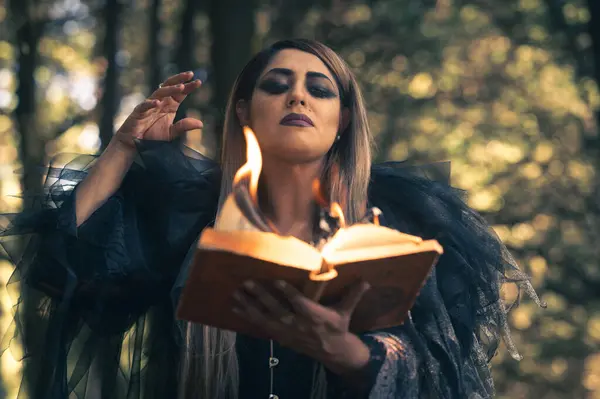 Sihirli büyü kitabıyla cadılar bayramı cadısı kız portresi. Cadı şapkalı güzel bir kadın sihirbazlık yapıyor. Ürkütücü kara büyü ormanlarında. Geniş Cadılar Bayramı parti sanat tasarımı.