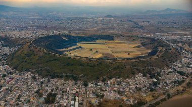 Drone aerial shot of the Xico Volcano, an extinct crater located in Chalco, State of Mexico. The image showcases the circular volcanic formation surrounded by urban settlements and agricultural fields clipart