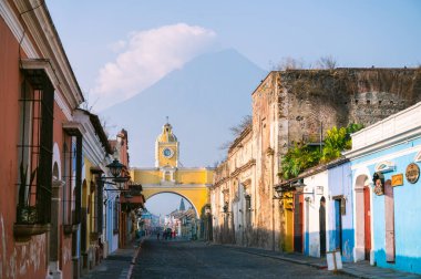 Antigua Guatemala 'daki ikonik Santa Catalina Kemeri' nin manzarası. Arka planda volkan var. Koloni binaları ve canlı renkler şehrin kültürel cazibesini yansıtıyor..