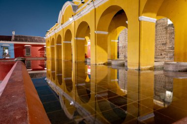 Antigua Guatemala 'daki Tanque La Union' ın gece görüşü bir zamanlar umumi çamaşır alanı olarak kullanılan berrak yıldızlı gökyüzünün altında ikonik sarı koloni kemerleri ve su yansımalarını gösteriyor..
