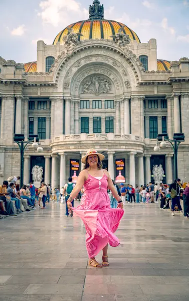 Sarı elbiseli zarif orta yaşlı kadın Torre Latinoamericana yakınlarında Meksiko 'yu keşfediyor, Palacio de Bellas Artes tarafından modern silueti ve arka planda tarihi heykeli ile yakalandı..