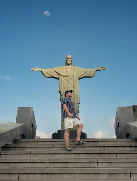 Erkek bir turist, Rio de Janeiro, Brezilya 'daki Kurtarıcı İsa' nın merdivenlerinde poz veriyor. Mavi gökyüzünde görünen ay, Güney Amerika 'daki sembolik ve simgesel bir seyahat anını yakalıyor..