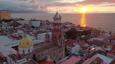 Meksika 'nın Puerto Vallarta kentindeki Guadalupe Hanımefendisi Kilisesi' nin ikonik panoramik görüntüsü. Kamera, deniz üzerinde nefes kesici bir günbatımını gözler önüne seriyor. Tarihi şehrin cazibesini vurguluyor.