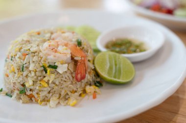 Shrimp fried rice on a white plate with fish sauce chili in a cup on the background of Thai food