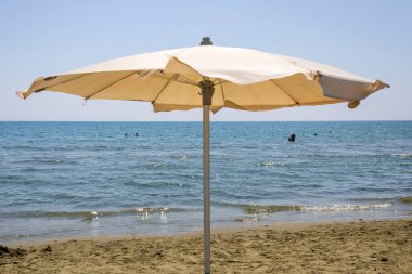 Mavi deniz ve gökyüzünün önündeki kumlu sahilde şemsiye, Kıbrıs