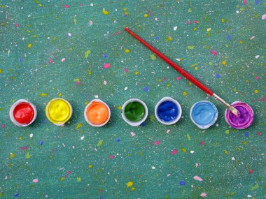 Soyut benekli yeşil arka planda çok renkli boya kapakları ve boya fırçası. 