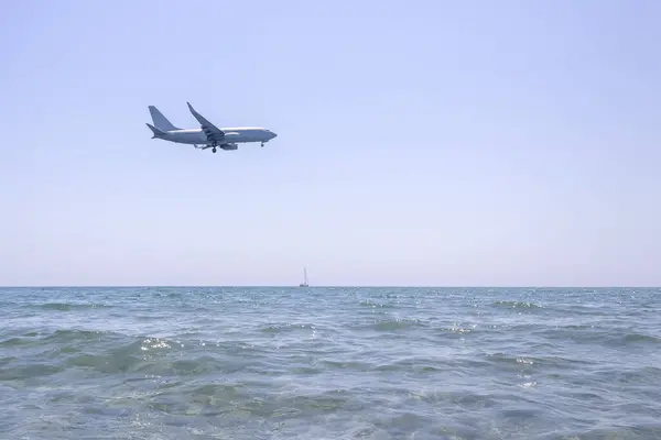 Passagierjet Fliegt Tief Strahlend Blauem Himmel Über Glänzendem Meer lizenzfreie Stockbilder