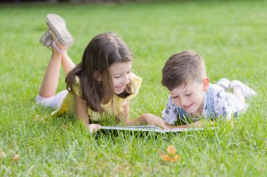 İki tatlı çocuk çimenlerde uzanıp kitap okuyorlar.