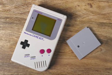 Neu-Ulm, Bavyera, Almanya - 26 Nisan 2023: İlk Nintendo Game Boy klasik versiyonu masada bir oyun kartuşunun yanında yatıyor.