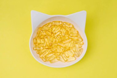 Sarı arka planda balık yağı Omega 3 haplarıyla dolu yüksek açılı beslenme çanağı manzarası.
