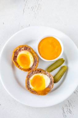 Portion of Scotch egg garnished with pickles and cheddar sauce