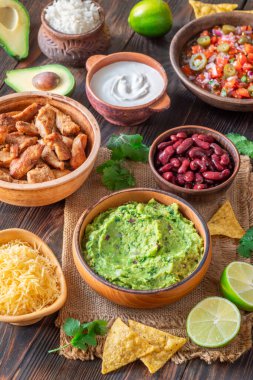 Burrito bileşenli kaseler: salsa, peynir, tavuk, ekşi krema, limon, kişniş, pirinç, guacamole, fasulye, avokado ve cips.