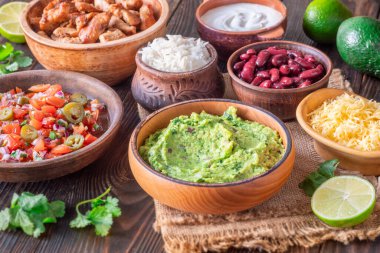 Burrito bileşenli kaseler: salsa, peynir, tavuk, ekşi krema, limon, kişniş, pirinç, guacamole, fasulye, avokado ve cips.