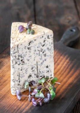 Kremalı, damarlı rokfor peyniri, kalın aromalı, ahşap bir tahtanın üzerine zarif bir şekilde yerleştirilmiş.