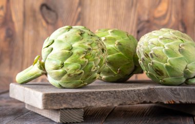 Yapraksı desenli çiğ enginarlar eski kesme tahtasına yaslanmış, kırsal bir ortam.