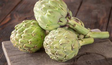 Yapraksı desenli çiğ enginarlar eski kesme tahtasına yaslanmış, kırsal bir ortam.