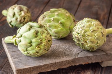 Yapraksı desenli çiğ enginarlar eski kesme tahtasına yaslanmış, kırsal bir ortam.