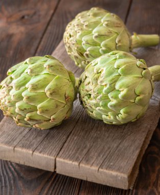 Yapraksı desenli çiğ enginarlar eski kesme tahtasına yaslanmış, kırsal bir ortam.