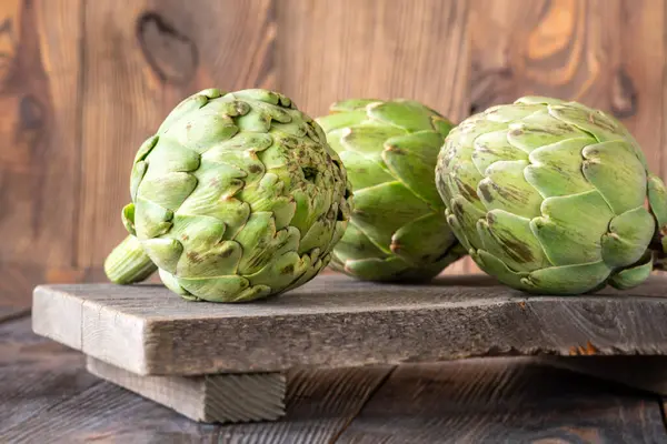 Yapraksı desenli çiğ enginarlar eski kesme tahtasına yaslanmış, kırsal bir ortam.