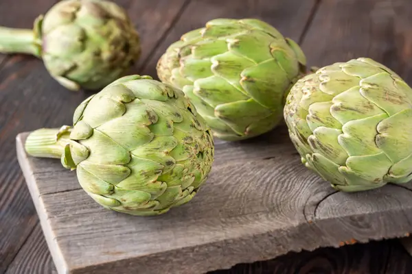 Yapraksı desenli çiğ enginarlar eski kesme tahtasına yaslanmış, kırsal bir ortam.