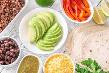 Canlı malzemeler ve dolgu malzemeleriyle çevrili tortillalar lezzetli tacoları bir araya getirmeye hazır.