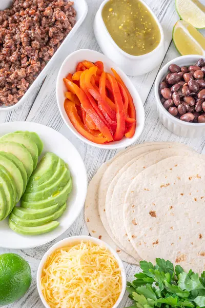Canlı malzemeler ve dolgu malzemeleriyle çevrili tortillalar lezzetli tacoları bir araya getirmeye hazır.