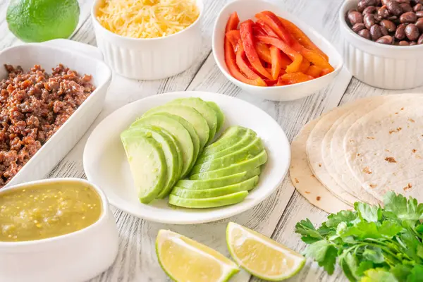 Canlı malzemeler ve dolgu malzemeleriyle çevrili tortillalar lezzetli tacoları bir araya getirmeye hazır.