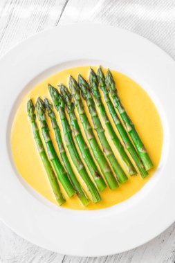 Zengin Hollandaise 'in tepesinde rafine edilmiş az pişmiş yeşil kuşkonmaz.