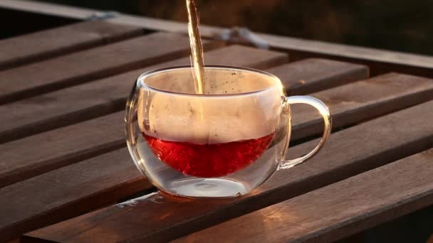朝食を提供するティーポットからの透明なガラス二重底のコップへの流れの新鮮な香りの熱い黒茶を注ぐクローズアップ 木のテーブル 優雅なマグの遅い動き — ストック動画