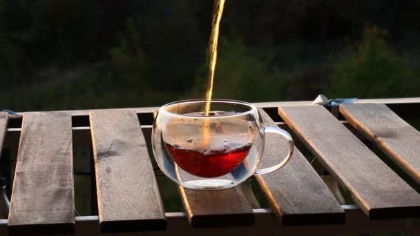 朝食を提供するティーポットからの透明なガラス二重底のコップへの流れの新鮮な香りの熱い黒茶を注ぐクローズアップ 木のテーブル 優雅なマグの遅い動き — ストック動画