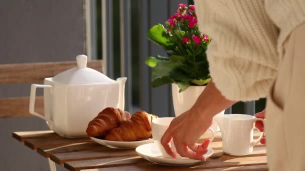 一个穿着白色毛衣的女人在桌子上摆满了茶和羊角面包 — 图库视频影像