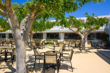 Kos, Yunanistan - 7 Mayıs 2023: Ağaçların altında masa ve sandalyeler bulunan rahat bir Yunan oteli terası. Kos Adası, Yunanistan