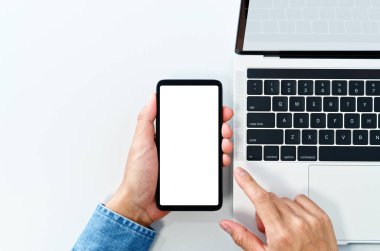Using smart phone from above. White blank screen. Laptop on white background