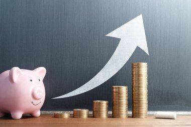 Increase savings. Concept image of saving money. Stack of coins and piggy bank. Arrow drawn on blackboard