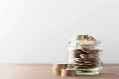 Saving money in jar. Jar filled with coins on wood table. Copy space