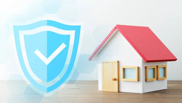 Home security system technology. Miniature house and shield icon with check mark. Wood table and white background