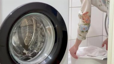 Yıkandıktan sonra ıslak beyaz elbiseler, kadınların elleri ıslak beyaz çamaşırları, ön planda çamaşır makinesini sıkar..