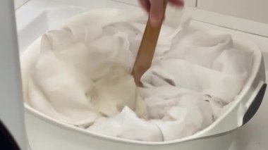 Ahşap maşayla Kirli Çamaşırları Sırılsıklam Etmek. Ahşap maşayla kirli beyaz elbiseleri karıştıran kadın elleri.
