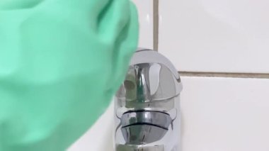 Banyodaki lavaboyu temizliyorum. Eldiven giyen bir kadın temizlik sırasında lavaboyu dezenfektanla yıkıyor...