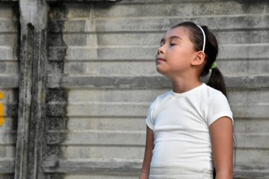 Duvarın yanında saç bandı takan Asyalı bir çocuk.