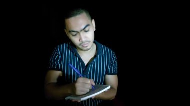 An Asian Man Writing In Notebook