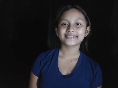 Mutlu Asyalı kız gülümsüyor ve kameraya gülümsüyor, siyah arkaplan