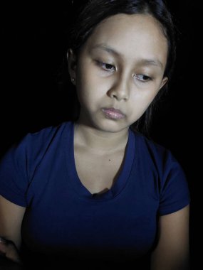 Üzgün Asyalı genç kız, koyu arkaplanda hüzün ifadesi var..